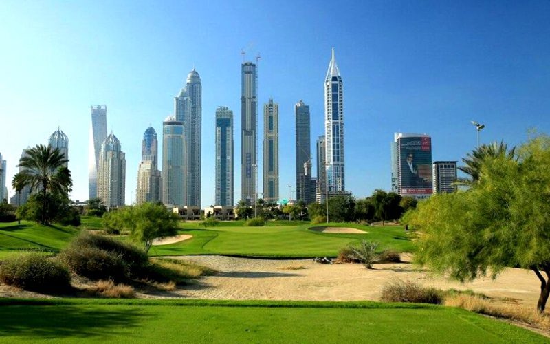 Lush green fairway at Emirates Golf Club’s Majlis Course with sand bunkers in the foreground and Dubai’s modern skyline of skyscrapers in the background under a clear blue sky.
