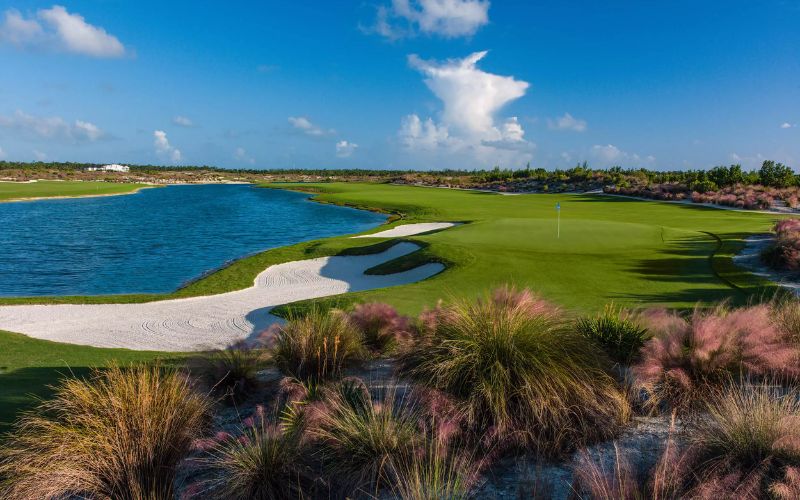 Albany Golf Course in New Providence, Bahamas, featuring green fairways along the ocean with palm trees, sand traps, and blue skies above