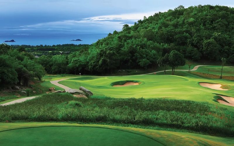 Banyan Golf Club in Hua Hin with lush green fairways, sand bunkers, and surrounding forested hills overlooking the sea.