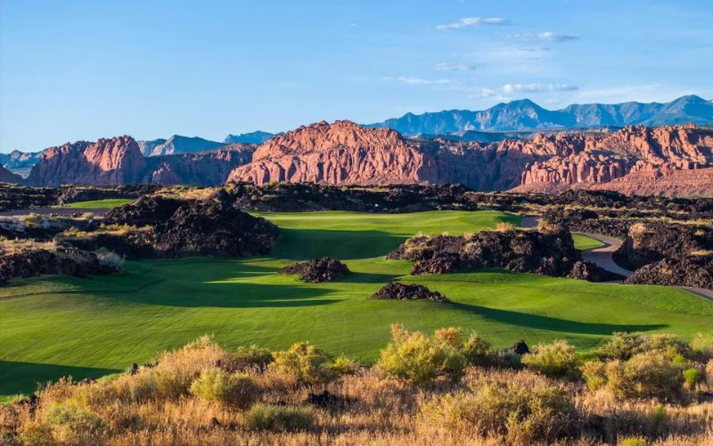 Golf course at Black Desert Resort in Ivins, Utah, with lush fairways surrounded by desert landscape and red sandstone cliffs under a blue sky