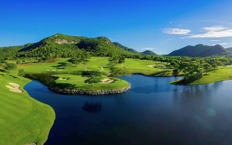 Black Mountain Golf Club in Hua Hin with pristine fairways, a large lake, and rolling green hills under clear blue skies.