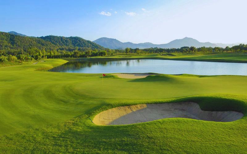Chiang Mai Highlands Golf & Spa Resort with lush fairways, sand bunkers, and a serene mountain backdrop beside a lake.