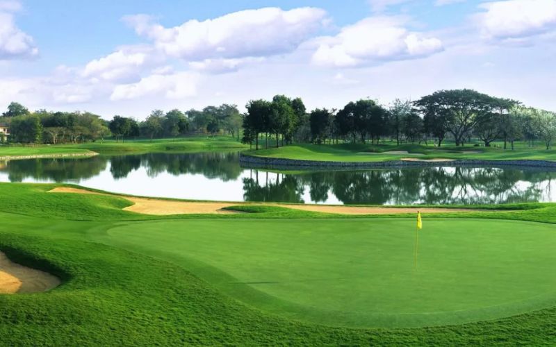 Peaceful view of Santiburi Country Club in Chiang Rai with lush green fairways, a lake, and distant mountain scenery.